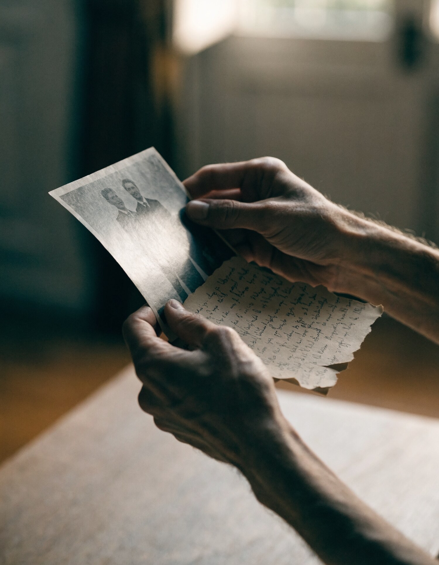 A pair of hands holding an old archival photograph and a worn handwritten letter
